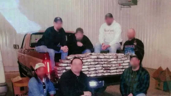 Major Crimes Unit members, faces blurred, behind a pickup truck bed stacked with packages of seized cocaine